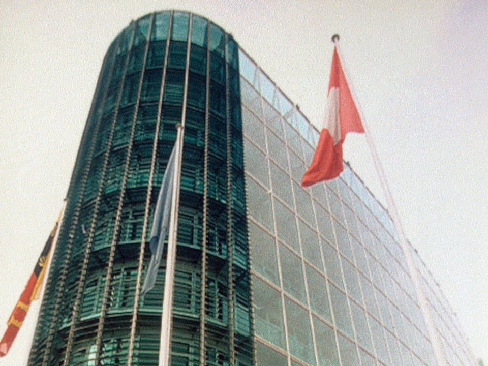 Ein grosses Glasgebäude mit einer Schweizer Fahne davor.