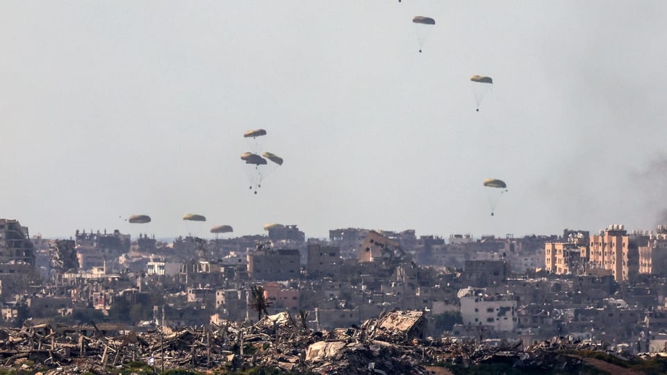 Hilfsgüter werden mit Fallschirmen über eine zerbombte Stadt geworfen. 