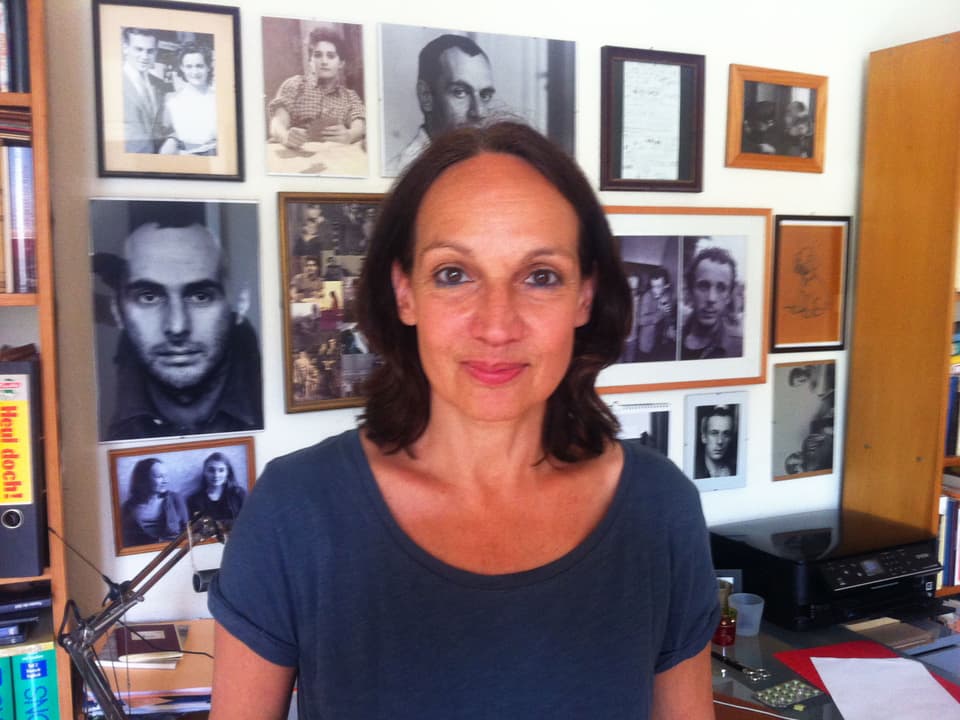 Mation Brasch in ihrem Arbeitszimmer. Im Hintergrund hängen Schwarz-Weiss-Fotos von verschiedenen Personen.