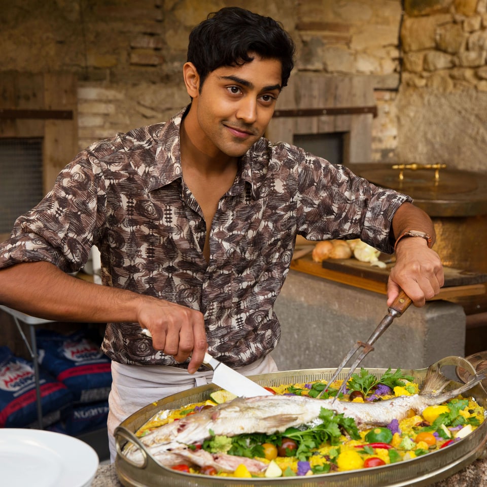 Indischer Koch schneidet Fisch in einem Paella-Kochtopf