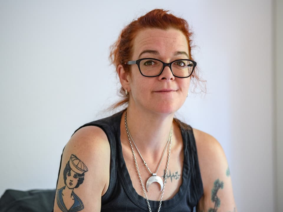 Frau mit roten Haaren, Brille und Tattoos auf den Armen.