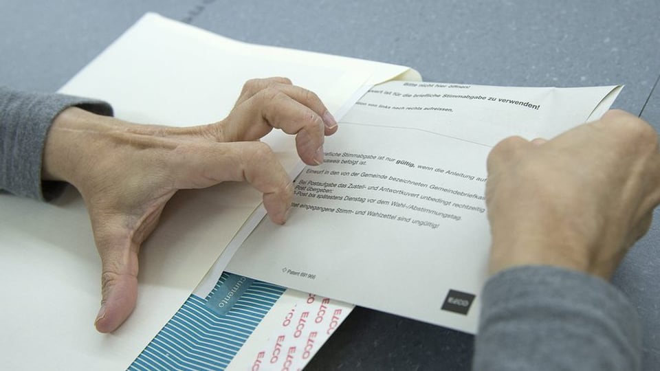 Eine Person steckt einen Stimmzettel in ein Wahlcouvert. 
