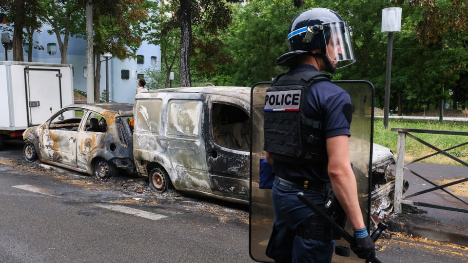 Ein französischer Polizist steht in Nanterre neben Fahrzeugen, 
