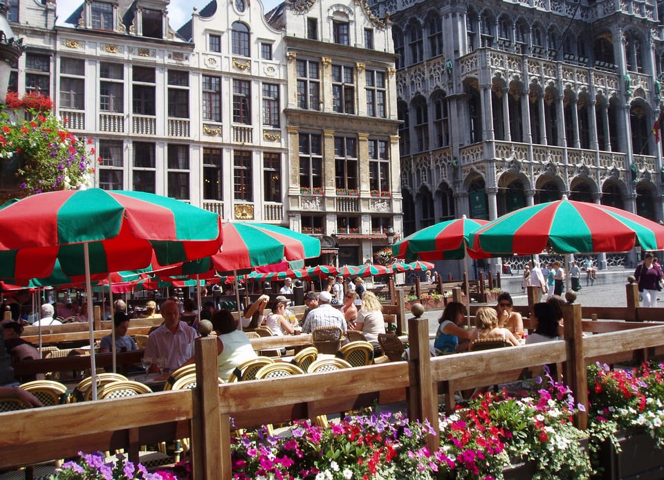 Menschen sitzen auf einem beschaulichen Platz in der Stadt Brüssel beisammen.