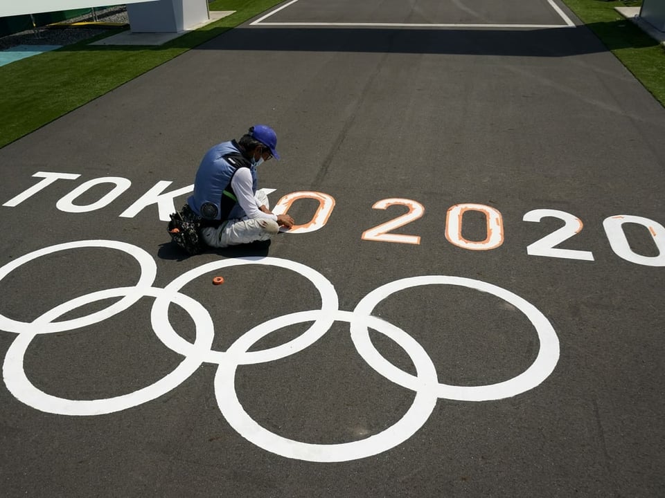 Person pinselt Logo der Olympischen Spiele in Tokio auf den Asphalt