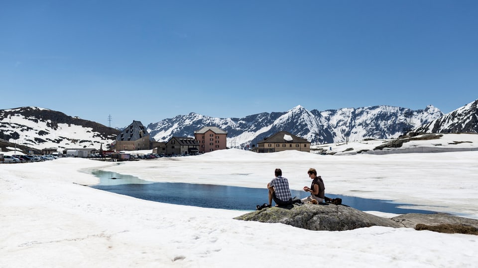 Zwei Menschen sitzen auf einem Stein im Schnee auf dem Gotthard-Pass.