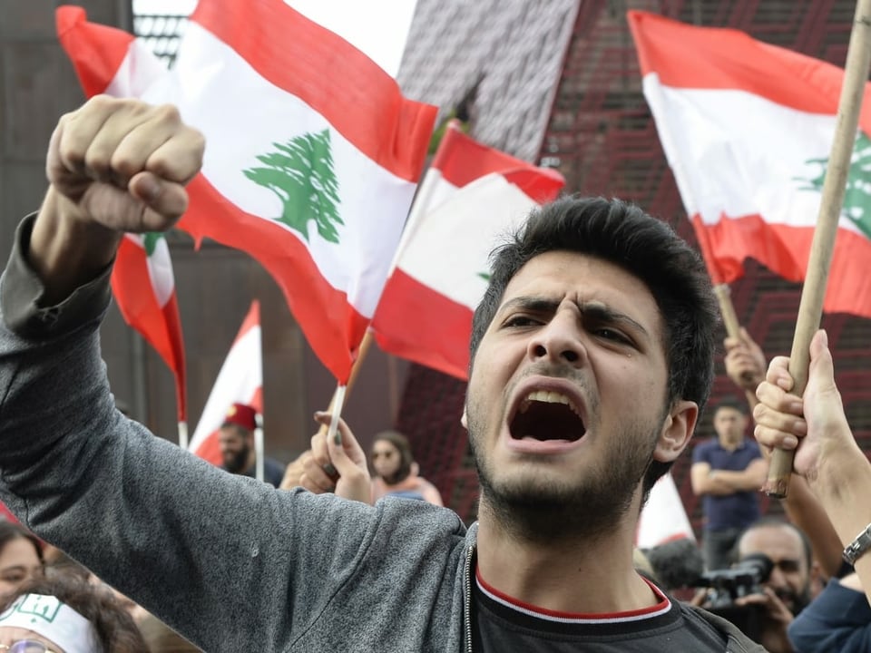 Ein junger Mann schreit mit erhobener Faust, im Hintergrund andere Demonstrierende mit Libanon-Flaggen
