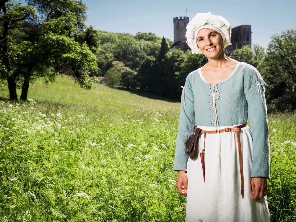 Frau in mittelalterlicher Kleidung auf einer Wiese mit einer Burg im Hintergrund