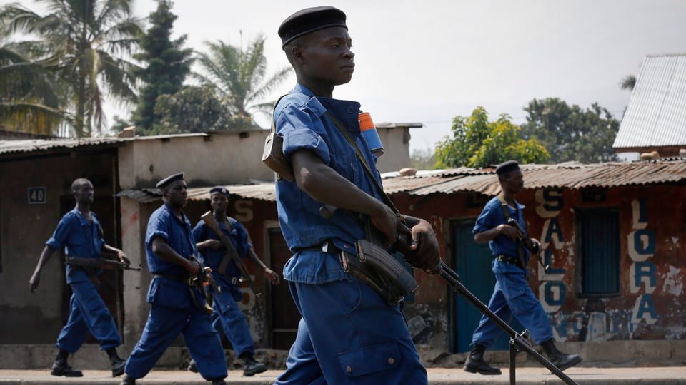 Fünf blau gekleidete burundische Polizisten mit Gewehren patrouillieren durch eine Strasse.