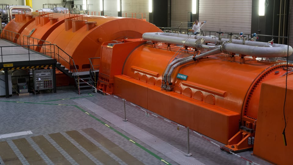 Eine grosse, orange, halbrunde Abdeckung ist zu sehen, darunter verborgen ist der Generator.