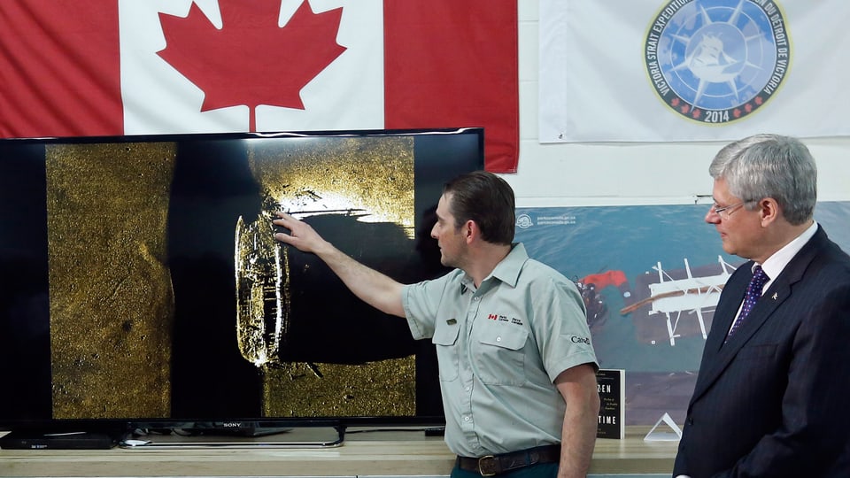 Kanadas Premierminister Stephen Harper rechts hört zu, wie ein Ranger von Parks Canada das Sonarbild mit dem Wrack der Franklin-Expedition erklärt.