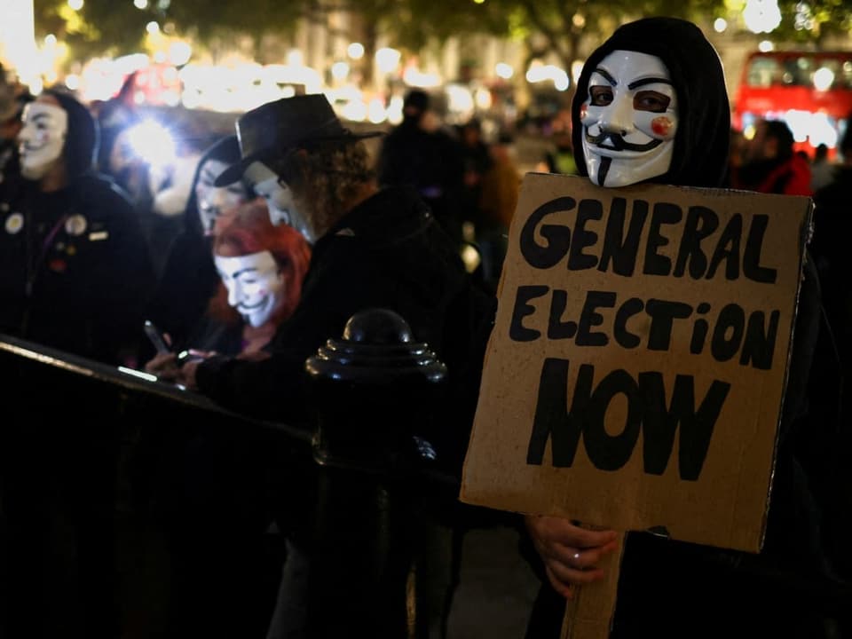 Ein Mann mit Maske hält ein Schild, dass Neuwahlen fordert.