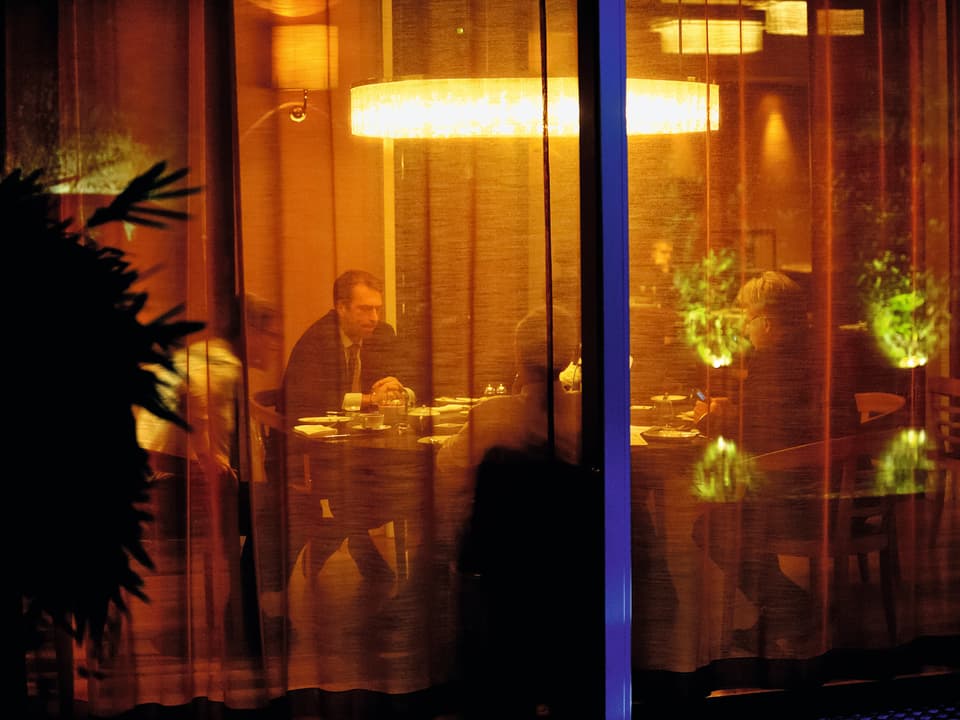 Männer sitzen an einem runten Tisch unter gelbem Licht.