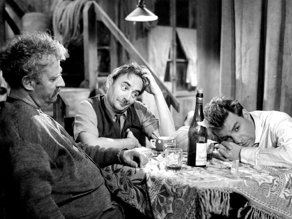 Drei Männer sitzen um einen Tischen und trinken Wein.