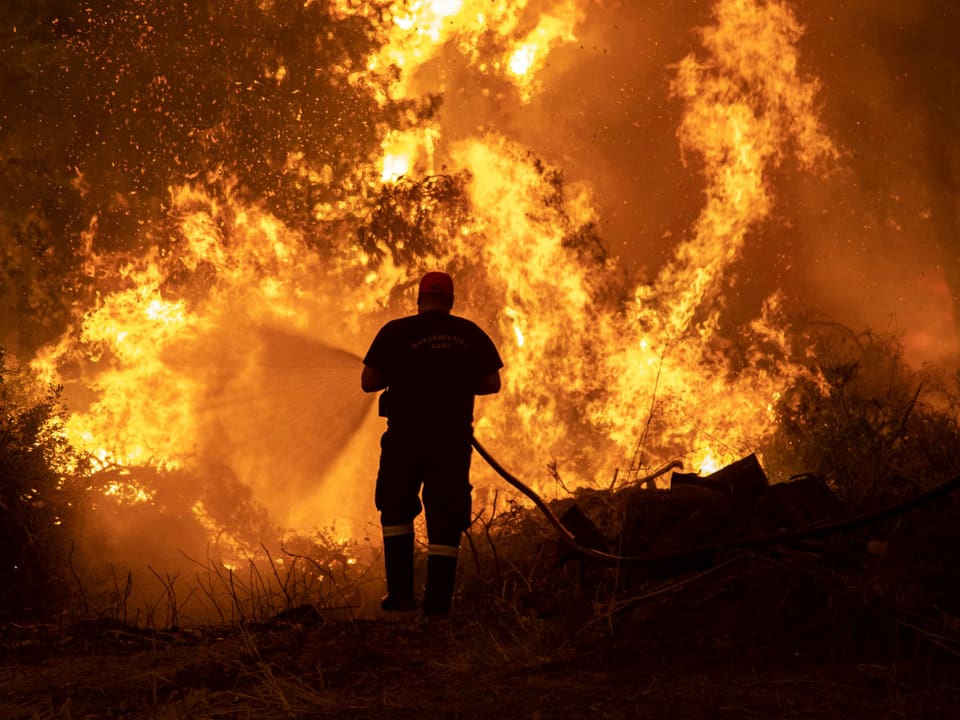 Ein Feuerwehrmann sprüht mit einem Schlauch Wasser auf ein grosses Feuer.