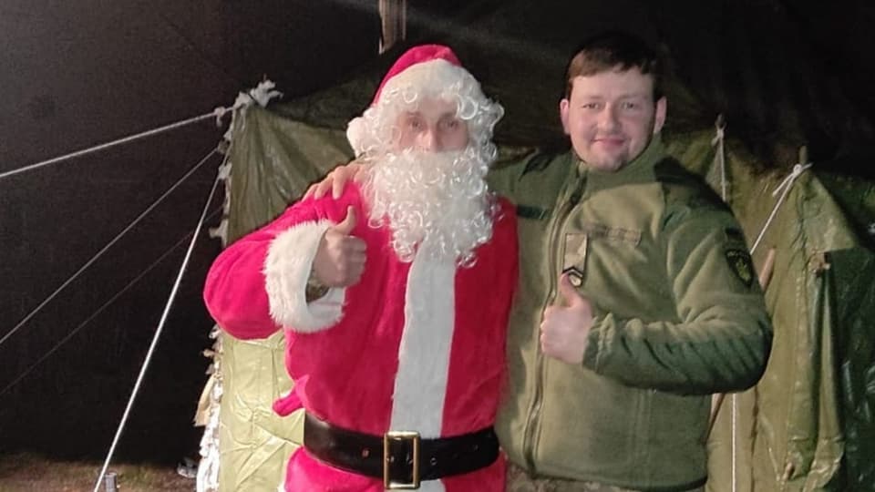 Ein als Weihnachtsmann verkleideter Soldat posiert mit einem Soldaten in Uniform vor einem Militärzelt.