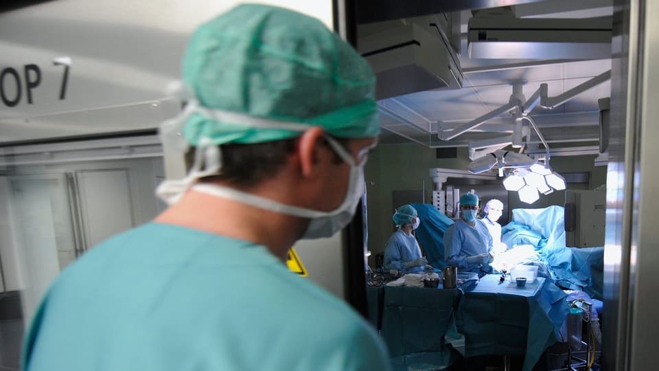 Ein Chirurg öffnet die Tür eines Operationssaals, wo seine Kollegen bereits an der Arbeit sind.