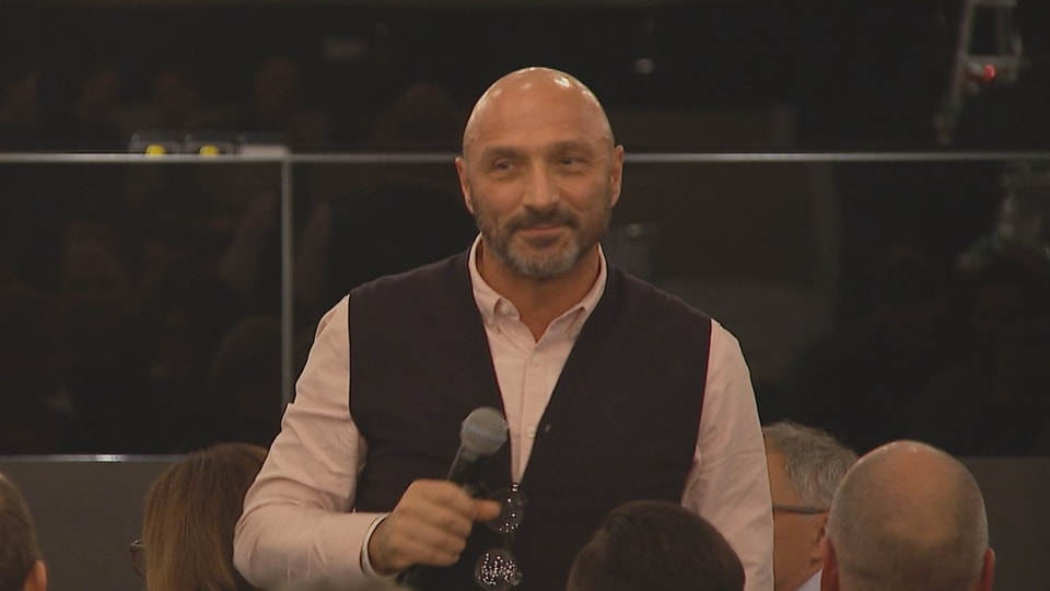 Massimo Ceccaroni hält ein Mikrofon in der Hand und hält vor mehreren Menschen einen Vortrag.