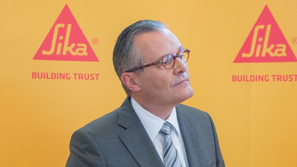 Sika-Präsident Paul Hälg an der diesjährigen GV vor einer gelben Wand mit zwei roten SIka-Logos