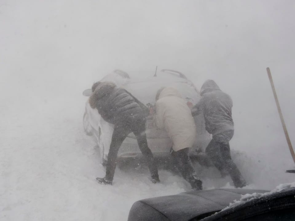 Drei Personen stossen Auto im Schneesturm an