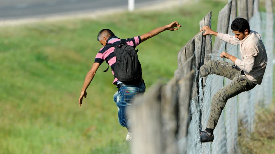 Männer klettern über einen Zaun