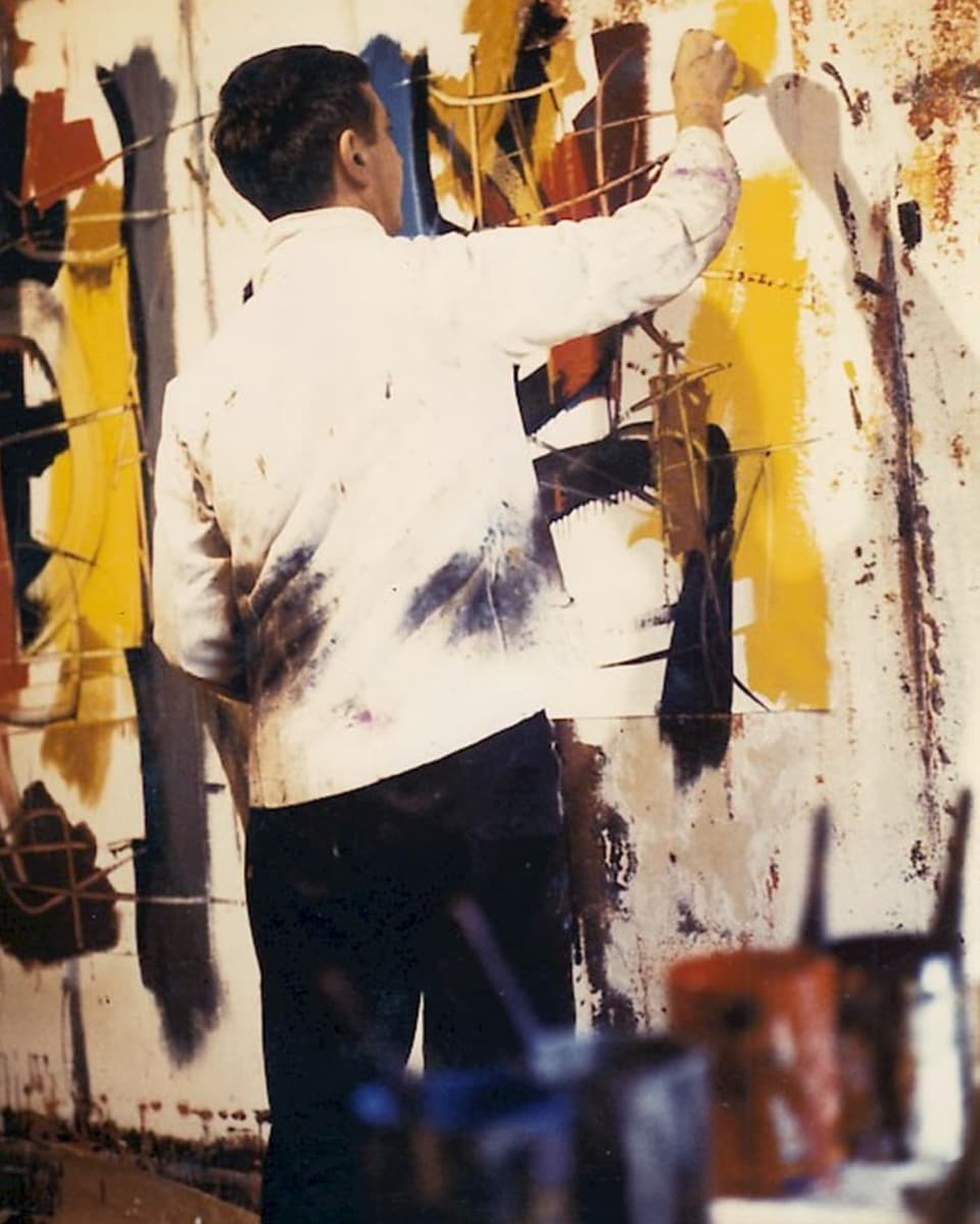 Ein Mann in weissem Hemd steht an einer bemalten Wand und bemalte diese mit gelber Farbe.