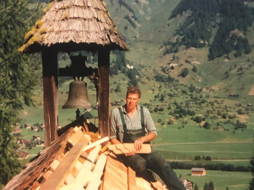 Ein junger Mann sitzt neben einem Stapel Holz auf dem Kirchendach.