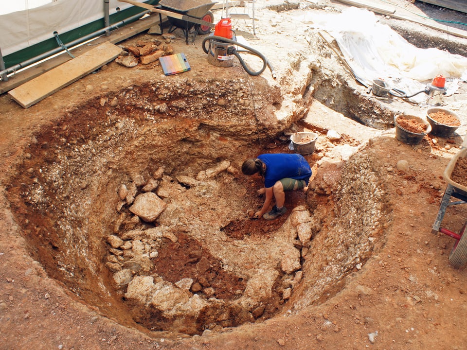 Archäologin arbeitet in runder Öffnung im Boden