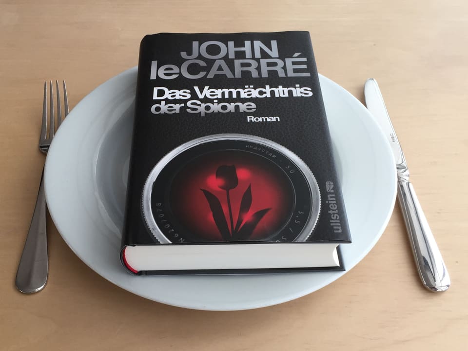 Der Roman «Das Vermächtnis der Spione» von John le Carré liegt auf einem weissen Teller. Messer und Gabel daneben.