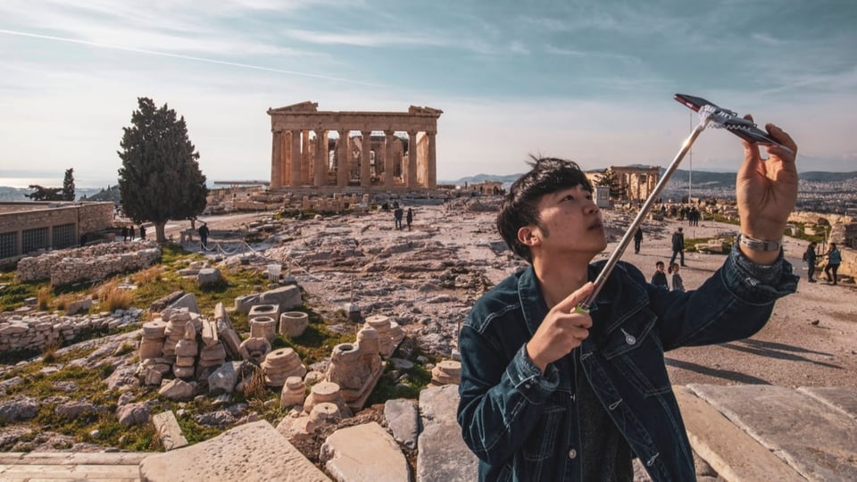 ein Mann macht ein Selfie vor der Akropolis in Athen.