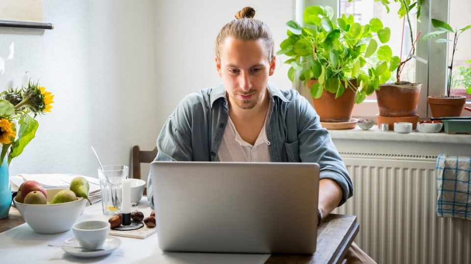 Junge lehnen sich über einen Tisch und schauen in einen Laptop.