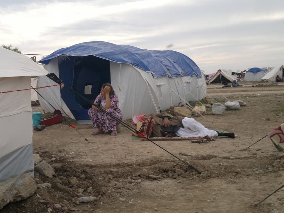 Eine Flüchtlingsfrau sitzt vor ihrem Zelt im Lager Khanke. Daneben liegt ein Mann auf einer Matte.