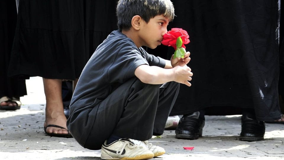Ein tamilischer Junge in den Kniene mit einer Nelke in der Hand.