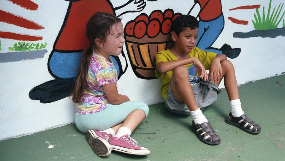 Zwei Kinder sitzen an eine Wand gelehnt am Boden.