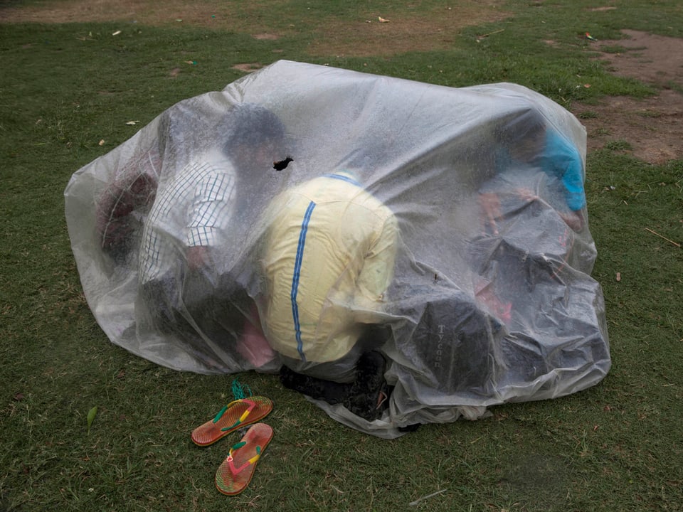 Mehrere Männer suchen unter einer Plastikhülle Schutz vor der Sonne
