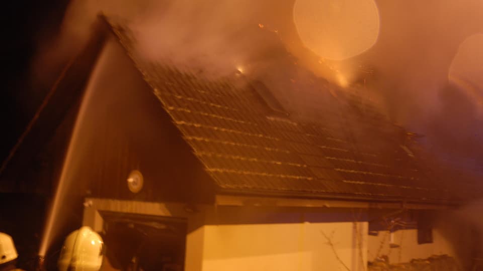 Feuerwehrmänner spritzen Wasser auf ein brennendes Hausdach.