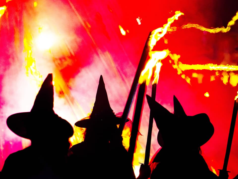 Dunkle Hexenhüte vor einem roten Hintergrund mit brennenden Fackeln