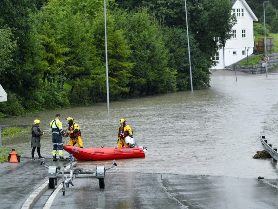 Eine überflutete Strasse. Davor stehen Rettungskräfte mit einem Boot. 