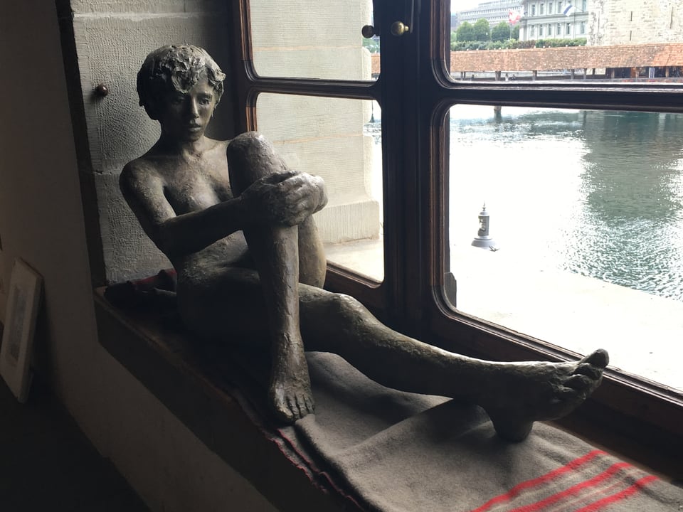 Eine Skulptur einer nakten Frau, die auf einem Fensterbank sitzt.