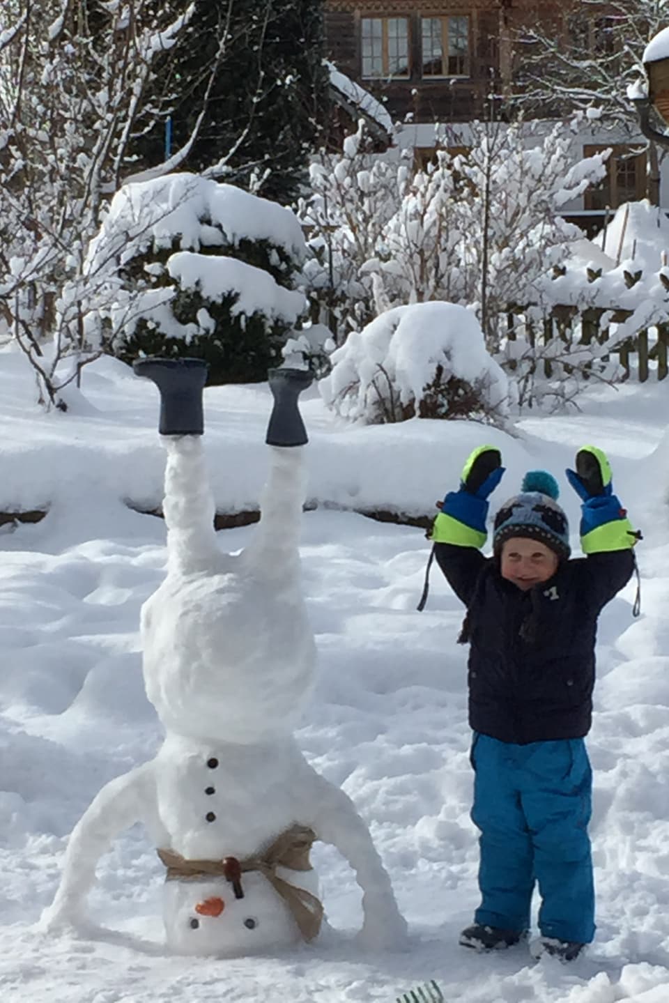 Links im Bild ein Schneemann, der den Kopfstand macht und seine Stiefel in den Himmel streckt. Rechts im Bild ein kleiner Junge, der seine beiden Arme in den Himmel streckt.
