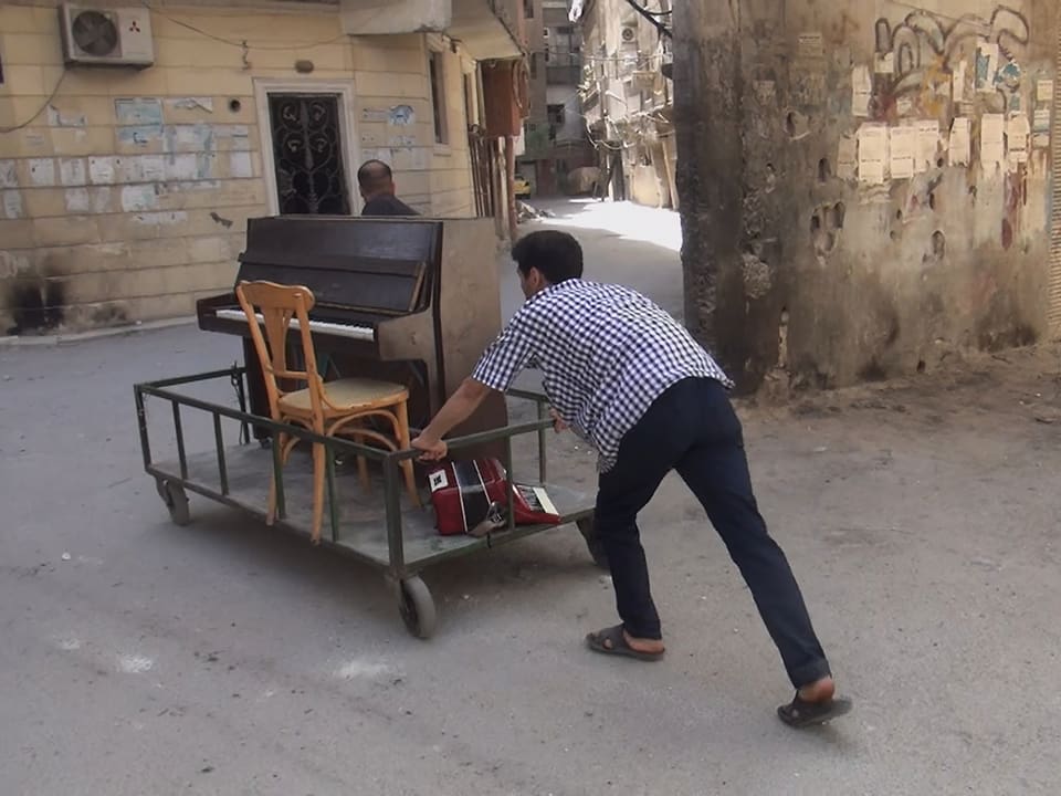 Ein Musiker schiebt ein Klavier durch die zerstörten Strassen Syriens.