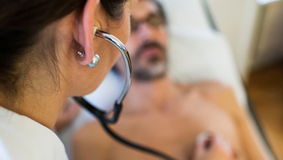Symbolbild: Eine Ärztin hört den Brustkorb eines Patienten ab, dieser liegt auf dem Untersuchungstisch.