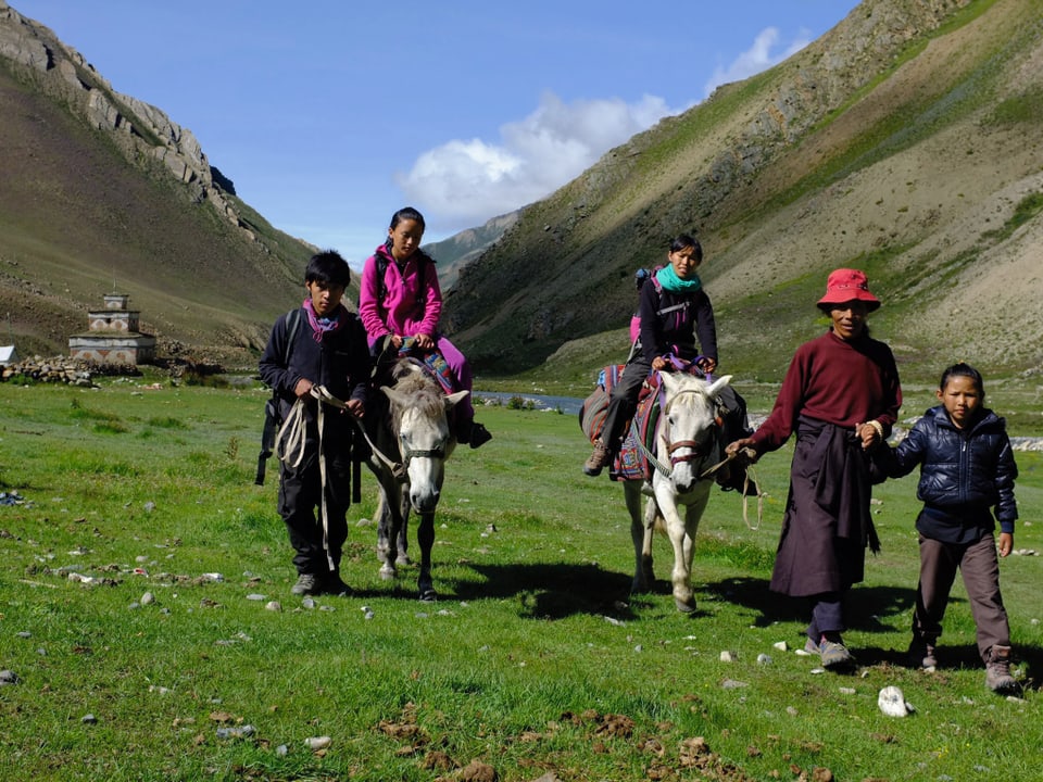 Pemain mit seiner Familie in einem grünen Tal in Nepal. Pemain und sein Vater führen je ein Pferd, auf dem jeweils eine seiner Schwestern sitzt. Die dritte, kleinste Schwester geht an der Hand ihres Vaters.