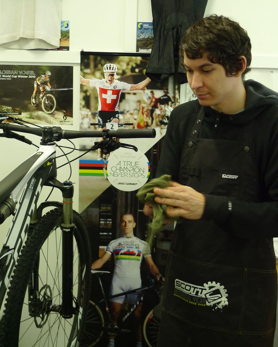 Zu sehen ist ein junger, ernster Mann der mit einem Lappen an einem aufgebockten Mountain-Bike steht. 