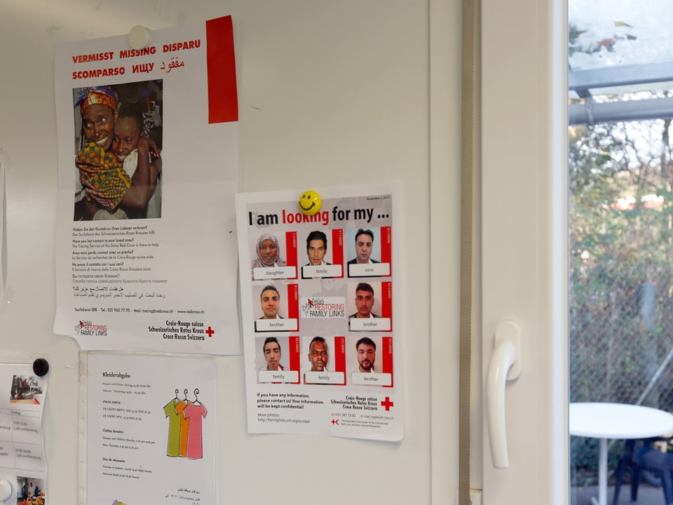 An einer Wand sind verschiedene Zettel angebracht, darunter einer vom Roten Kreuz, der mit einem Aufruf versucht, vermisste Menschen zusammenzubringen. 