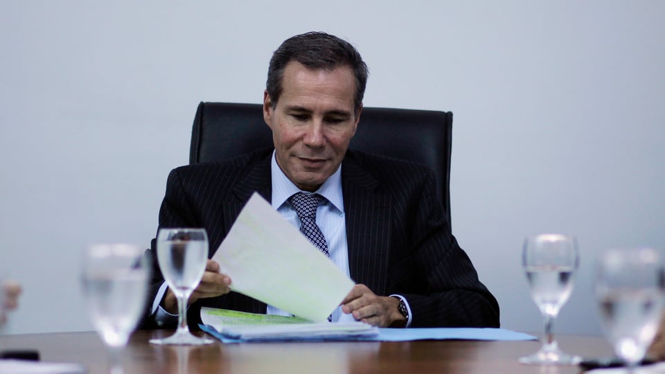 Ein Mann im Anzug sitzt an einem Tisch, in seinen Händen hält er Dokumente