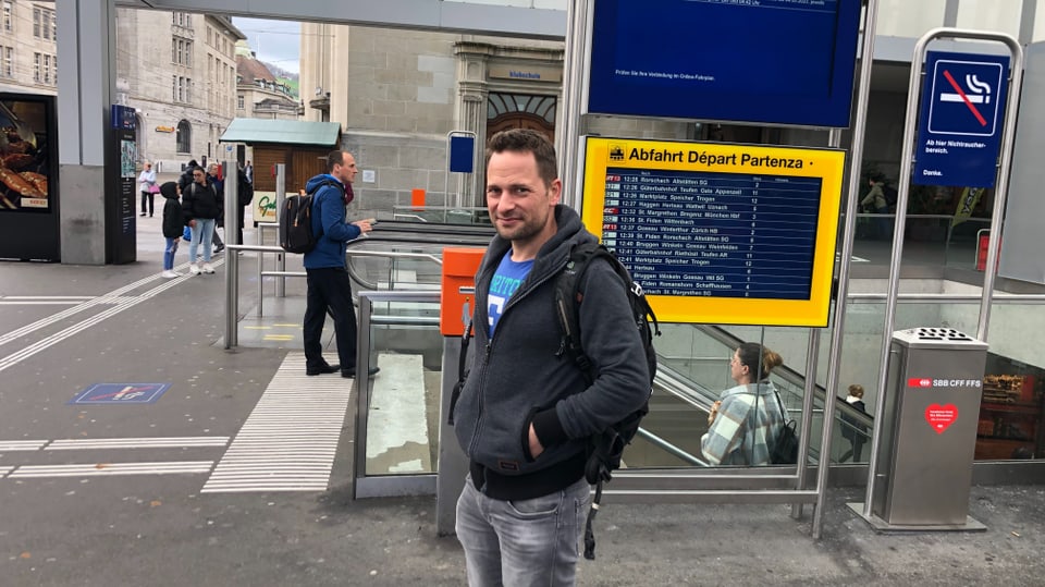 David Widmer steht am Bahnhof St. Gallen und wartet vor der Anzeigetafel auf den Zug. 