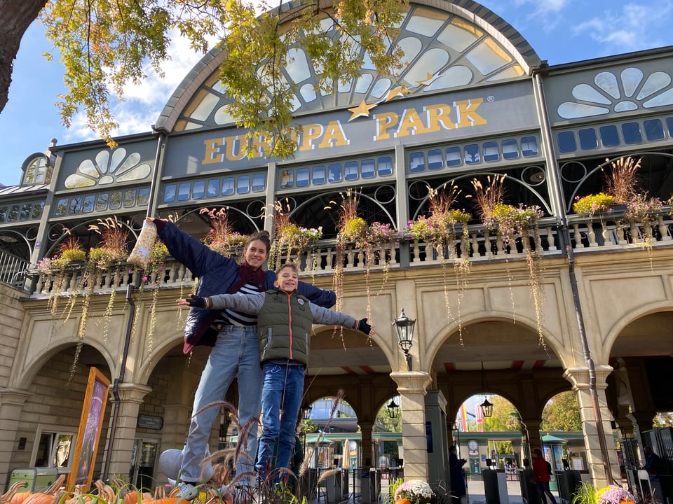 Dania und Nick posieren mit ausgestreckten Armen vor dem Eingang des Europaparks.