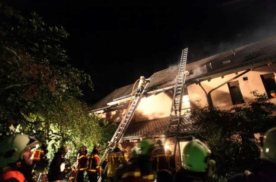 Die Feuerwehr stellt Leitern auf ein Mehrfamilienhaus, um ein Brand zu löschen.