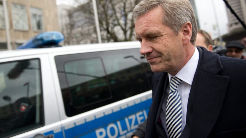 Wulf an einem Polizeiauto vorbeigehend.